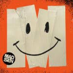 Die Illustration zeigt ein lächelndes Gesicht, das aus Klebeband auf orangefarbenem Hintergrund geformt ist. Unten links im Bild ist ein kreisförmiges Logo mit der Aufschrift "MADSEN".